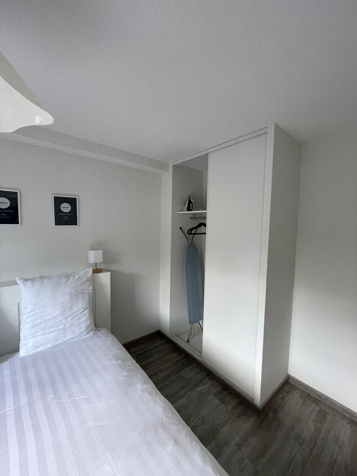 Une chambre d’hôtel équipée d’un lit, d’une armoire, d’un miroir et d’une planche à repasser fixée au mur.