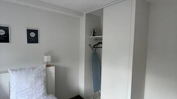 A hotel room with a bed, a wardrobe, a mirror, and a wall-mounted ironing board.