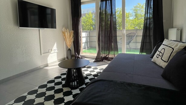 Habitación de hotel moderna con una cama grande, un televisor de pantalla plana en la pared, una pequeña mesa redonda y vistas al exterior a través de una puerta corrediza de vidrio.
