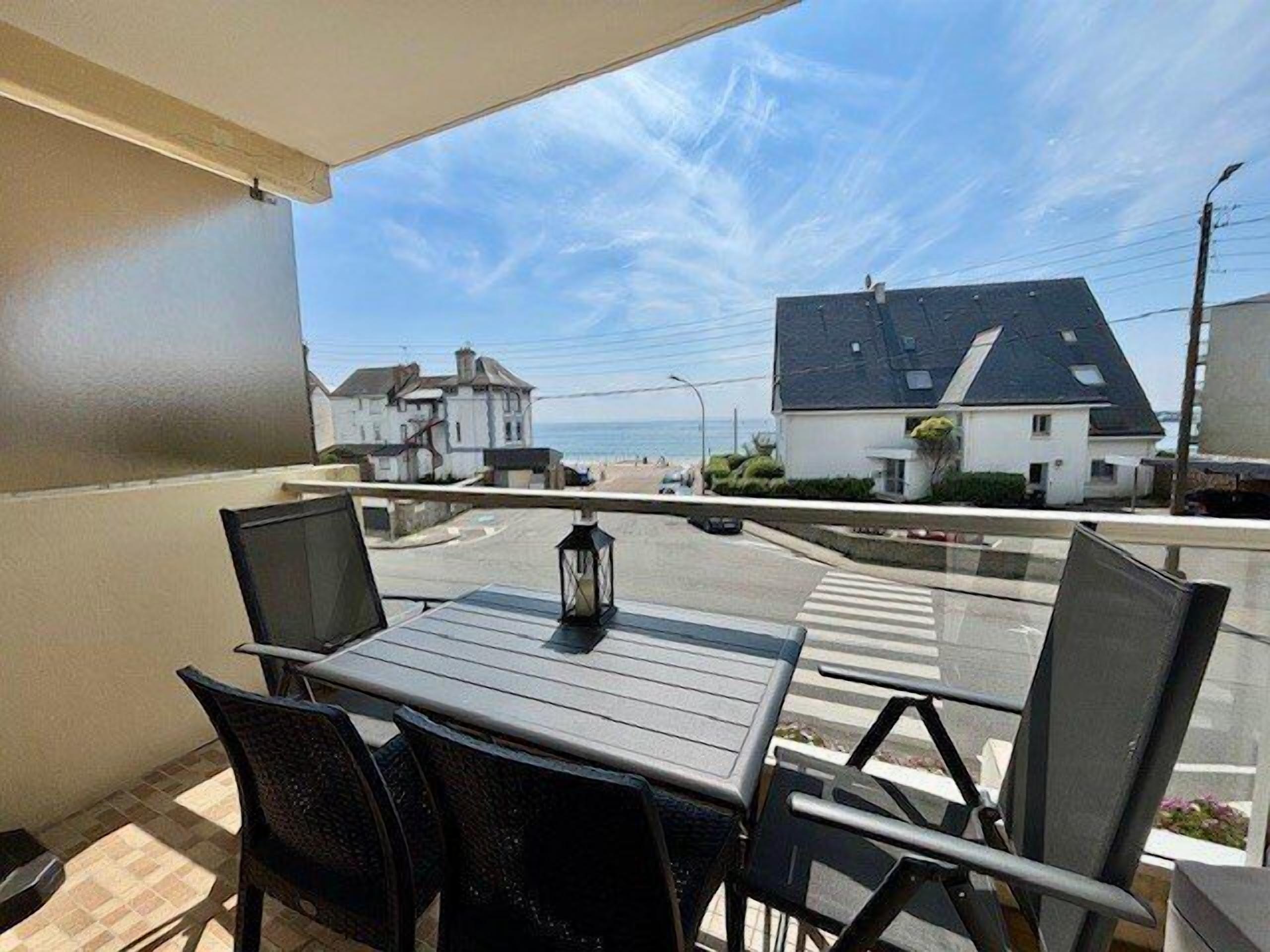 A balcony with a table and chairs, overlooking a street with houses and a clear sky.