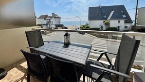 Un balcon avec une table et des chaises, donnant sur une rue bordée de maisons et offrant une vue sur un ciel dégagé.