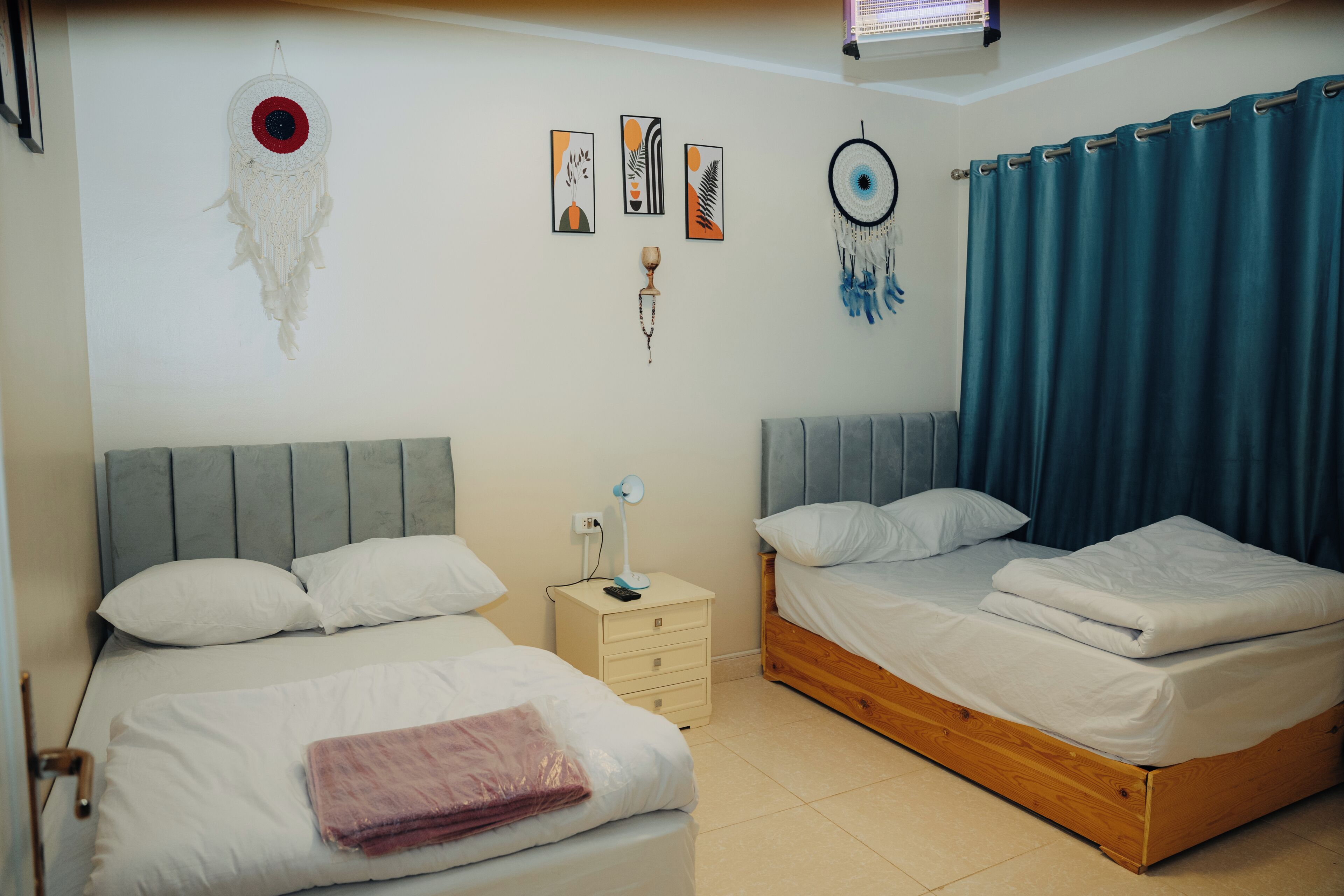 Ein Schlafzimmer mit zwei Betten, einem Nachttisch mit Lampe sowie Wanddekorationen, darunter Traumfänger und Bilderrahmen.