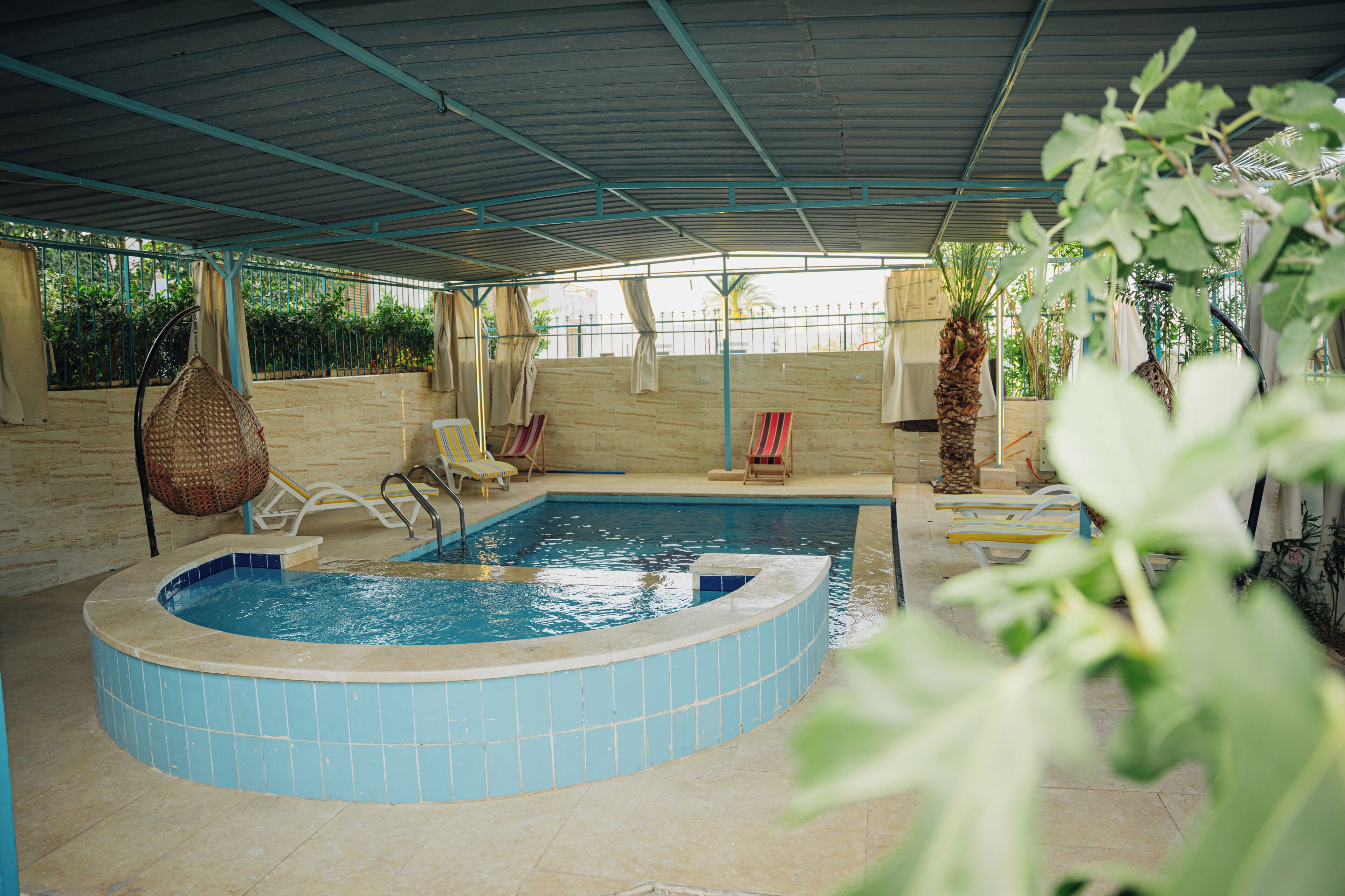 An indoor swimming pool with a tiled edge, surrounded by lounge chairs and a covered roof structure.