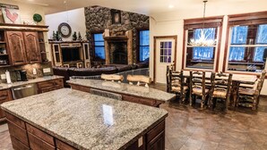 A spacious kitchen with granite countertops, wooden cabinets, and a stone fireplace.