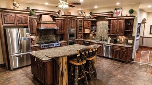 A kitchen with wooden cabinets, stainless steel appliances, a granite countertop, and a central island with stools.