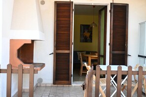 A patio with a table and chairs, a wooden bench, and a door with shutters.