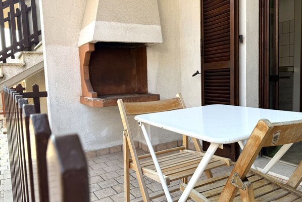 A patio with a table and chairs, a brick oven, and a wooden fence.