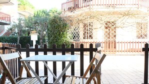 An outdoor seating area with a table and chairs, a wooden fence, and a building with a balcony in the background. - M421 - Marcelli, two-room apartment with patio 100m from the sea (Marcelli)