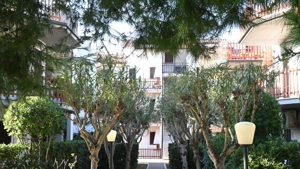 A pathway flanked by trees and lamp posts, leading to a building with balconies. - M421 - Marcelli, two-room apartment with patio 100m from the sea (Marcelli)
