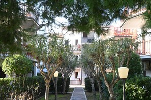 A pathway flanked by trees and lamp posts, leading to a building with balconies.