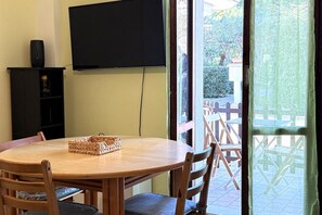 A round wooden table with chairs, a television mounted on the wall, and a sliding glass door leading to an outdoor area with a wooden fence.