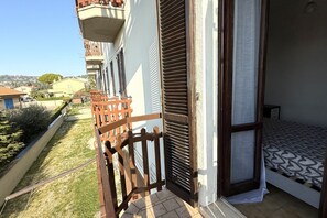 Un balcon avec une balustrade en bois, une persienne fermée et un lit avec une literie à motifs.