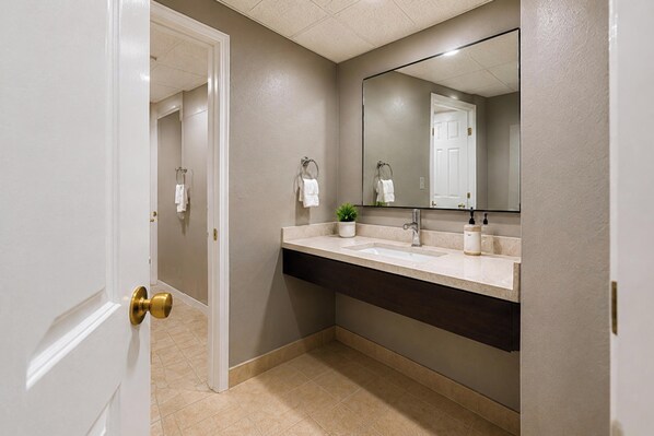 A bathroom with a white door, a sink with a dark countertop, a mirror, and a potted plant. - Cumberland Inn By Oyo New Cumberland/Hershey South (Camp Hill)