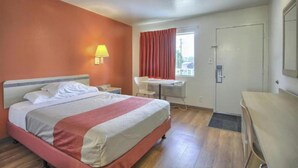Une chambre d’hôtel avec un lit, un bureau, une chaise, une fenêtre avec des rideaux et une porte.