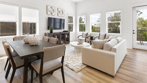 A spacious living room with a wooden dining table, beige sofa, and large windows. - Easy Street | New Home | 7 Beds | Pool | Golf Cart | Bikes (Santa Rosa Beach)