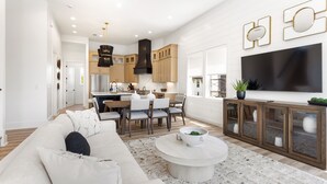 A modern living room with a white sofa, a coffee table, and a TV mounted on the wall. - Easy Street | New Home | 7 Beds | Pool | Golf Cart | Bikes (Santa Rosa Beach)
