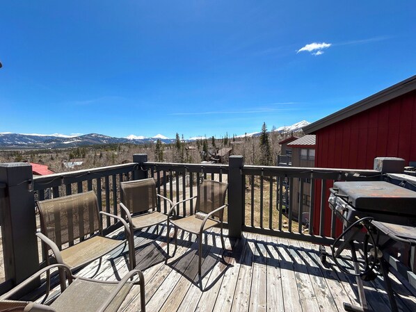 Une terrasse en bois, dotée de mobilier d’extérieur et d’un barbecue, offrant une vue sur un paysage montagneux.