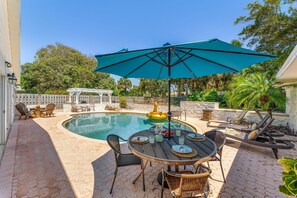 Un espace piscine avec une table ronde, des chaises et un grand parasol.