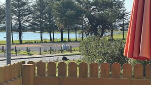 A wooden fence with a decorative knot, a metal gate, and a view of a lake with trees and a road in the background.