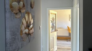 A hallway with a wooden floor, a door with a stained glass design, and a wall with a floral artwork.