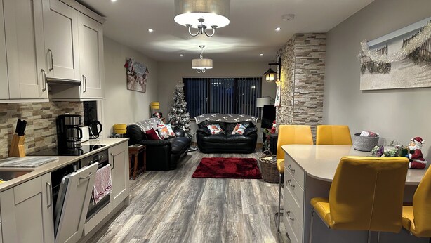 A modern kitchen with white cabinets, a dining area with yellow chairs, a black leather sofa, and a Christmas tree.