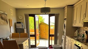 A modern kitchen with wooden flooring, a dining area with a table and chairs, and a view of the backyard through glass doors.