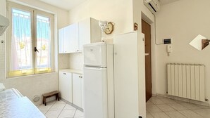 Een keuken met witte kastjes, een koelkast, een klok en een raam met gordijnen.