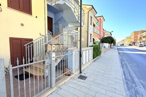 A residential building with a staircase, a metal fence, and a sidewalk.