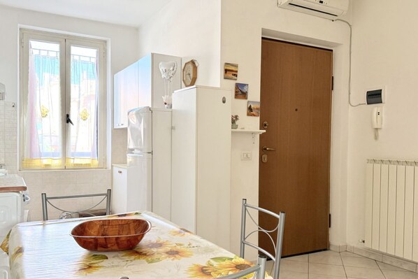 A kitchen with a dining table, chairs, a refrigerator, and a wooden door.