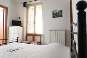 A bedroom with a bed, a dresser, a chair, a radiator, a window with curtains, and a painting on the wall.