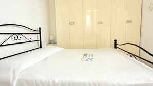 Een enkel bed met een metalen frame, een wit sprei en een garderobe met spiegel en lichtschakelaar.