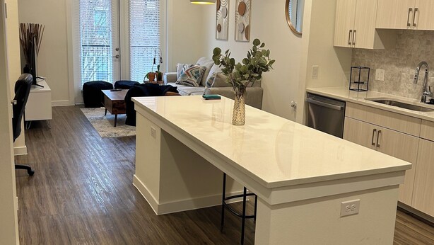 A modern kitchen with a central island, pendant lighting, and a dining area with a sofa and chairs.
