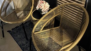 Two wicker chairs with a small table and a vase of flowers between them, placed on a patterned rug.