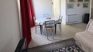 A room with a dining table, chairs, a bed, a radiator, and framed pictures on the wall.