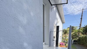 A set of concrete steps leading to a white door, a metal handrail, and a small garden area with plants and a chair.
