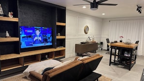 Ein modernes Wohnzimmer mit Fernseher, Sofa, Couchtisch und einem Essbereich mit Tisch und Stühlen.