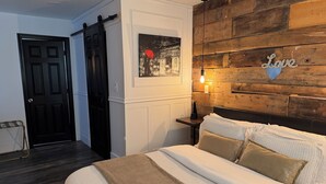 Ein Schlafzimmer mit hölzernem Kopfteil, einem Bett mit weißer Bettwäsche, einem Nachttisch mit Lampe und einem gerahmten Bild an der Wand.