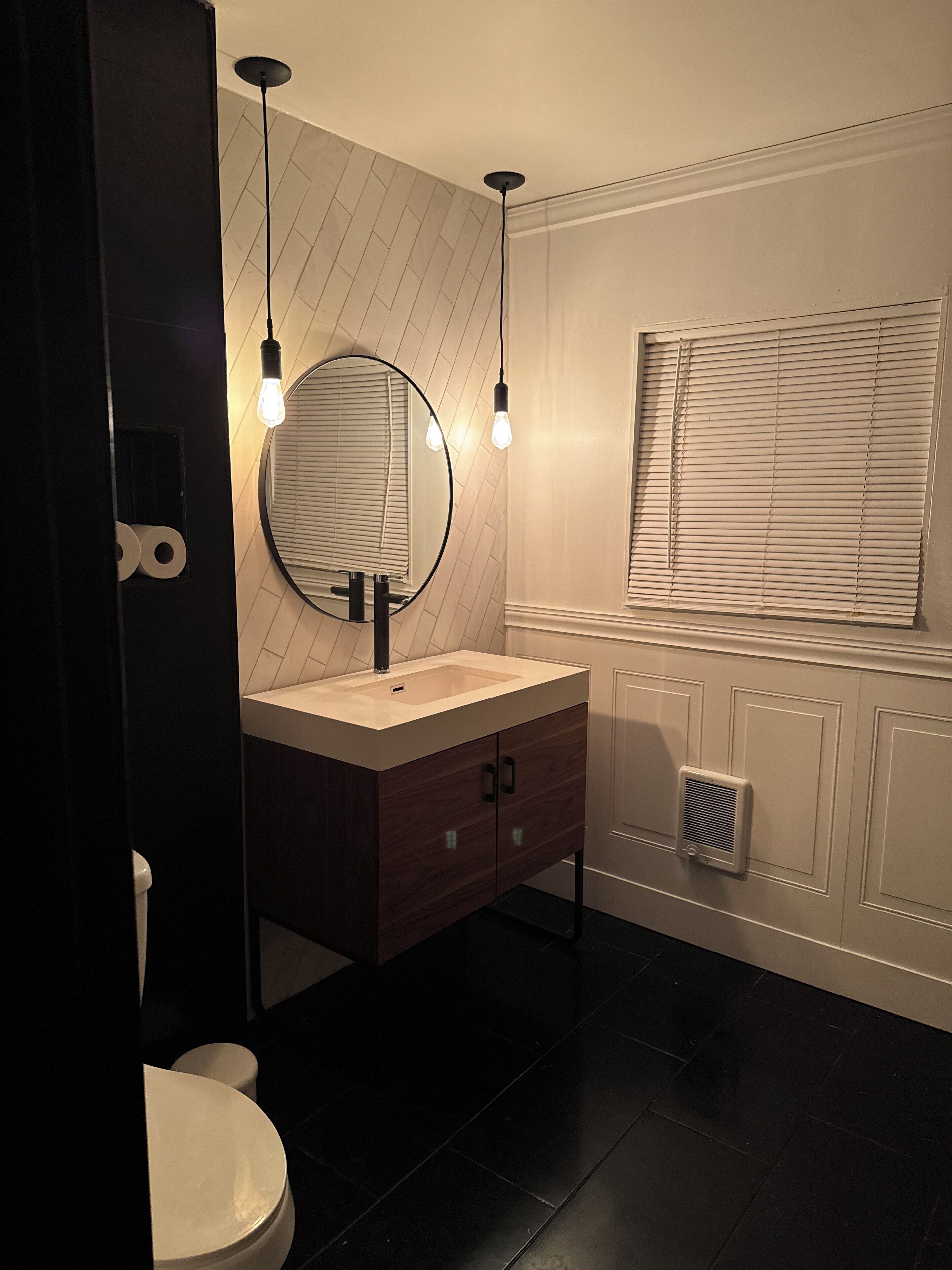 Een moderne badkamer met een ronde spiegel, een wastafel en een toilet. Boven de spiegel hangen twee hanglampen.
