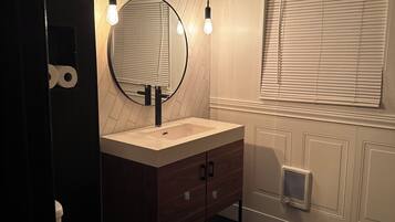 Een moderne badkamer met een ronde spiegel, een wastafel en een toilet. Boven de spiegel hangen twee hanglampen.