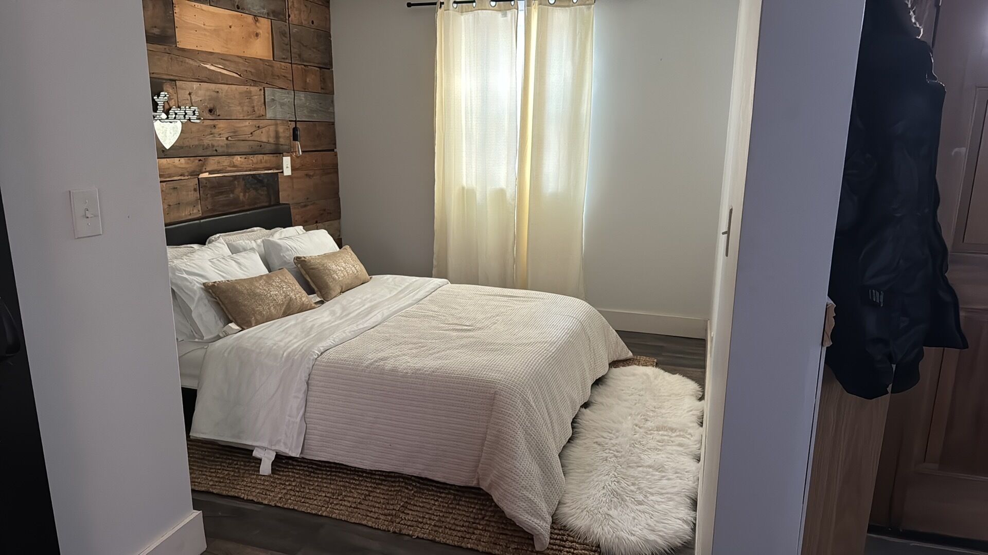A bedroom with a bed, white bedding, a fluffy rug, and a wooden wall.