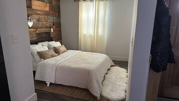 A bedroom with a bed, white bedding, a fluffy rug, and a wooden wall.
