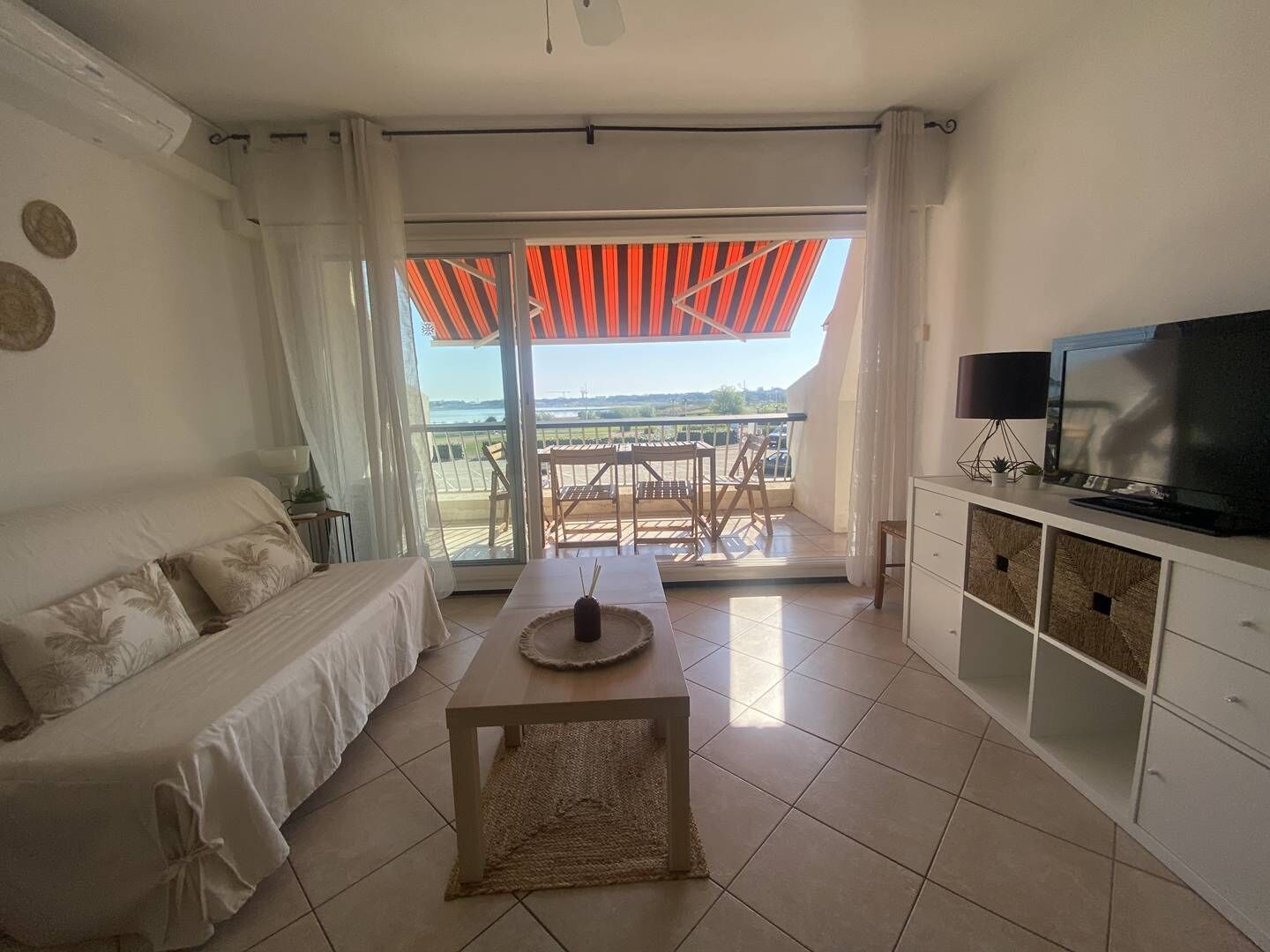A modern living room with a sofa, a coffee table, a TV, and a balcony with a view.