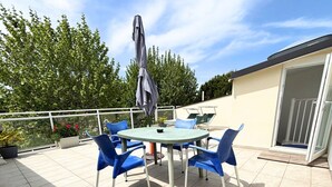 Ein runder Tisch mit vier blauen Stühlen, einem grauen Sonnenschirm und einer Glastür, die auf einen Balkon führt.