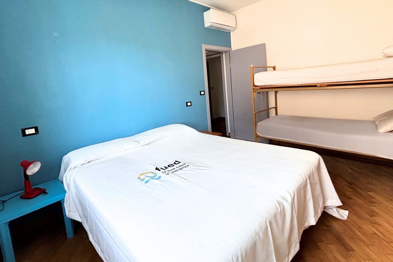 Een kamer met een stapelbed, een eenpersoonsbed, een bureau met lamp en een wandairconditioner.