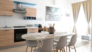 Une cuisine moderne avec des meubles en bois, une cuisinière à gaz et un coin repas comprenant une table et des chaises en verre.