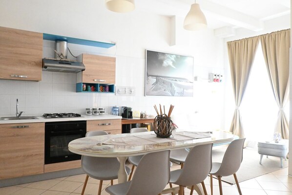 A modern kitchen with wooden cabinets, a gas stove, and a dining area with a glass table and chairs.