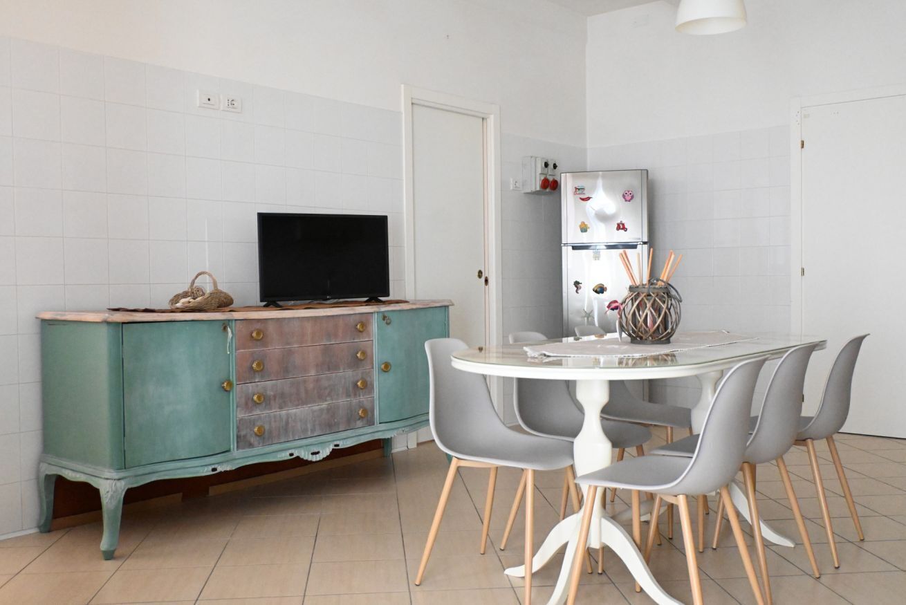 A kitchen with a teal cabinet, a black TV, a white refrigerator, and a round dining table with grey chairs.