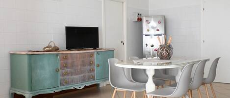 A kitchen with a teal cabinet, a black TV, a white refrigerator, and a round dining table with grey chairs.