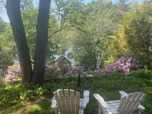 Zwei Adirondack-Stühle in einem Garten mit Bäumen und blühenden Sträuchern.