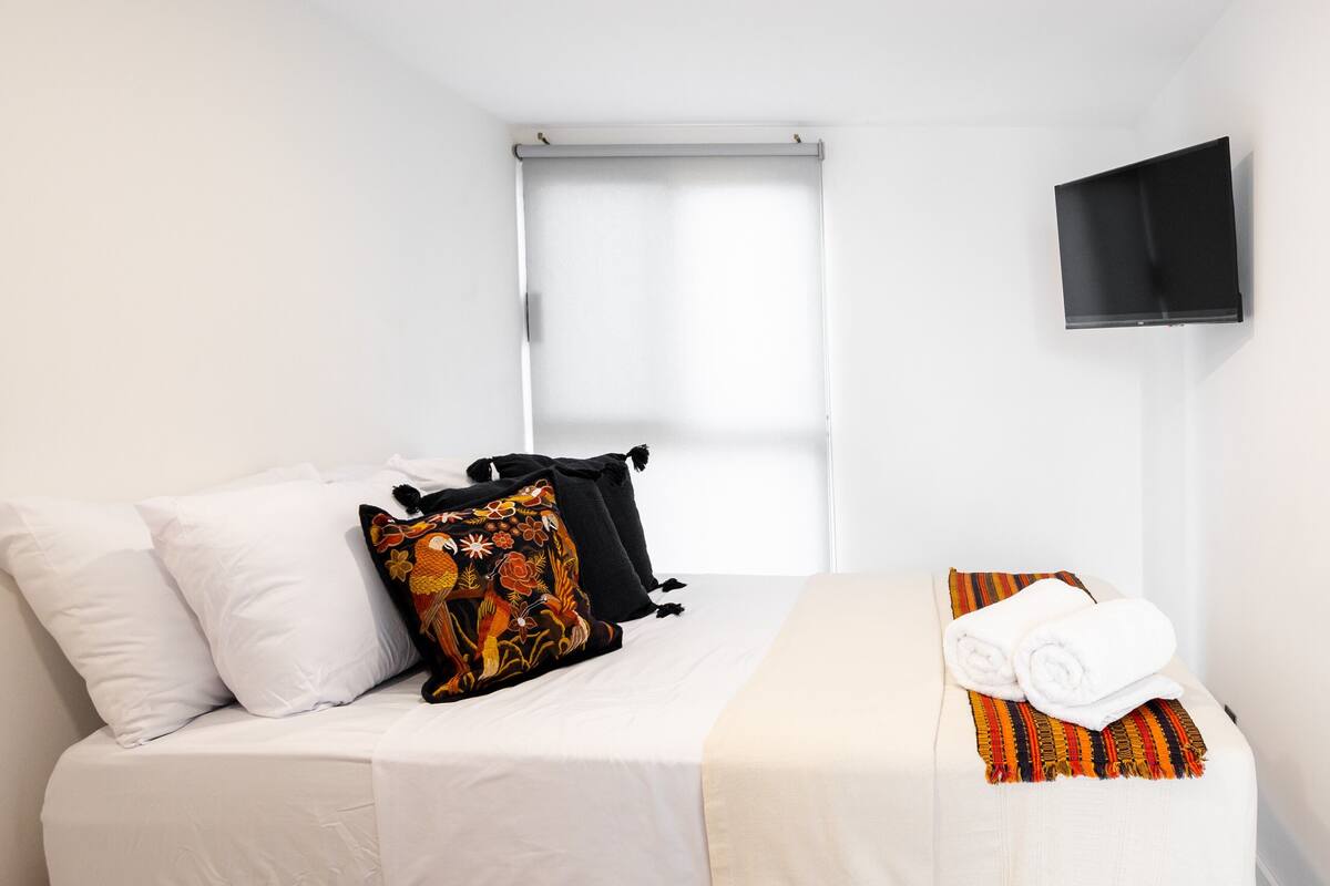 Une chambre d’hôtel avec un lit, des oreillers, une couverture, une télévision et une fenêtre.